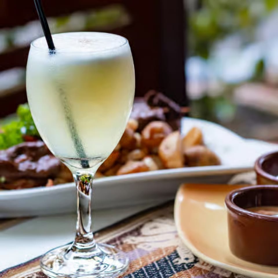 A refreshing cocktail with a black straw, next to a plate of food and small dipping bowls.