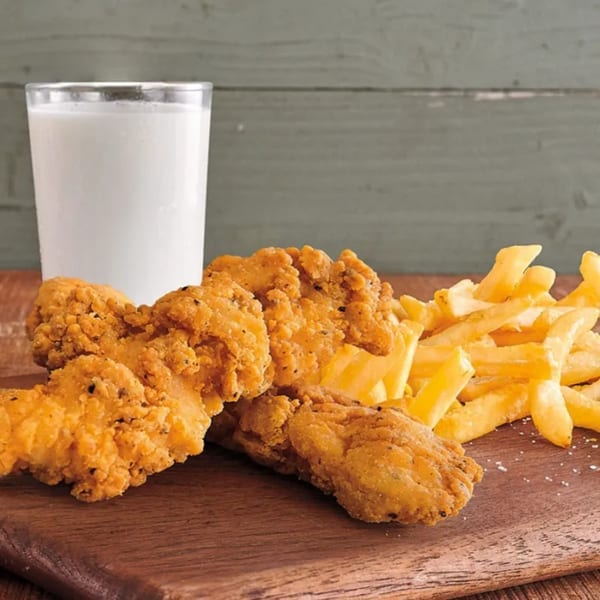 Golden fried chicken tenders and french fries on a wooden board with a glass of milk.