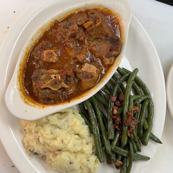 Oxtail stew in a white dish, with mashed potatoes and green beans topped with bacon bits.