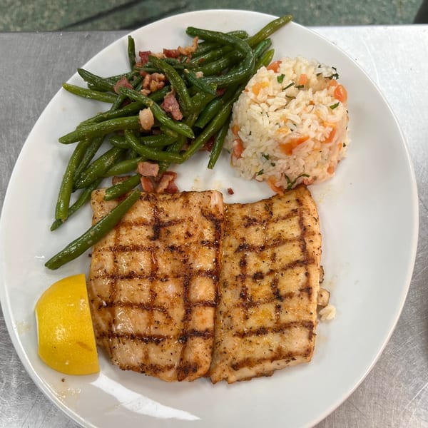 Grilled fish with green beans, rice, and a lemon wedge on a white plate.