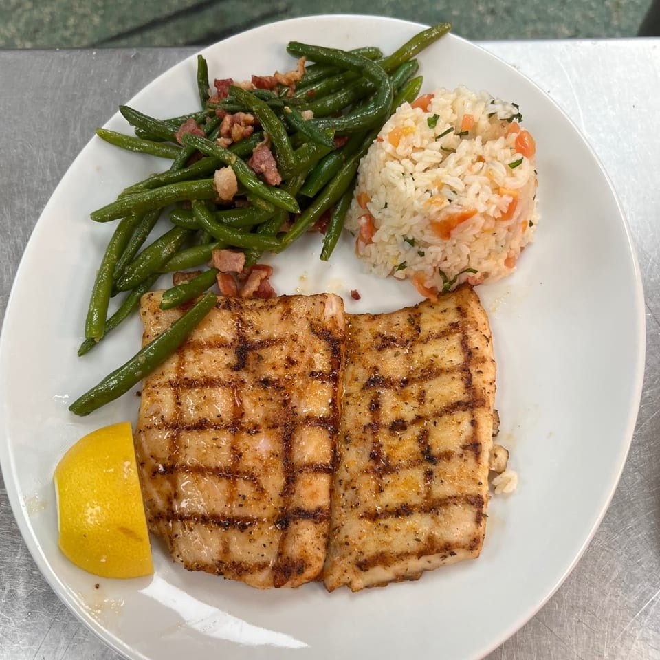 Grilled fish with green beans, rice, and a lemon wedge on a white plate.