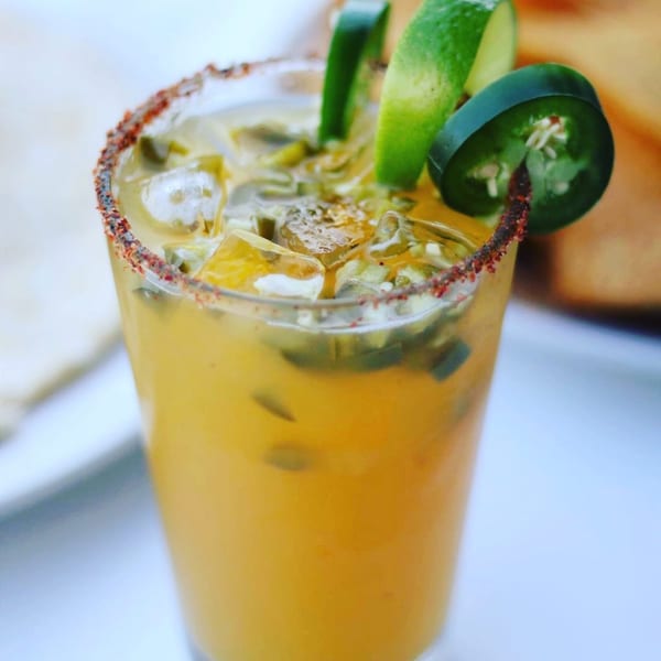 Spicy mango margarita with a chili-lime rim, garnished with lime wedges and jalapeño slices.
