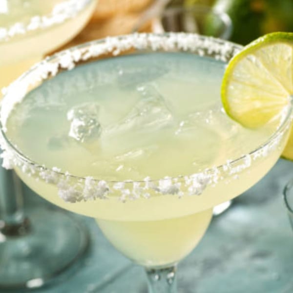 Close-up of a margarita with a salted rim and a lime wedge, filled with ice.